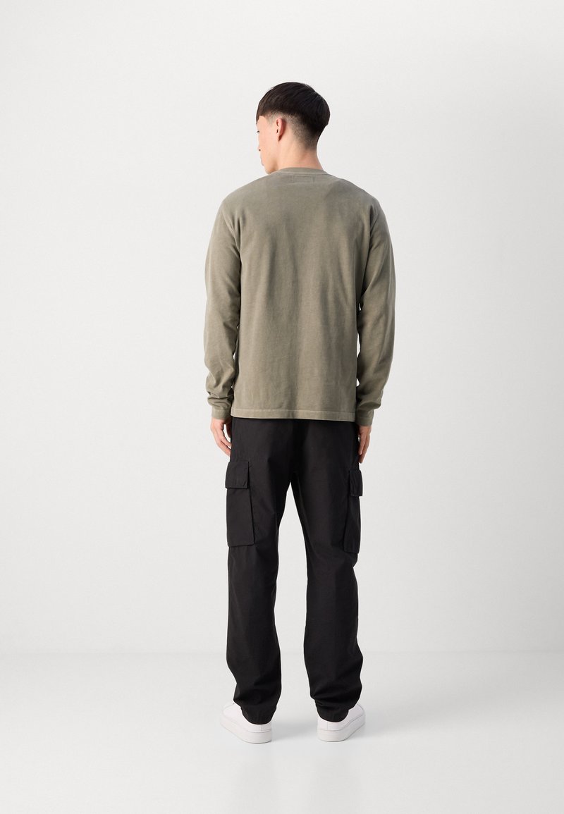 Chemise olive verte à manches longues, en tissu coton, coupe décontractée, col rond. Pantalons cargo noirs, texture douce, poches latérales, associés à des baskets blanches.