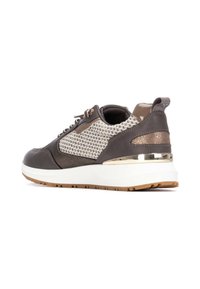 Zapatilla deportiva gris con parte superior de punto, detalles de cuero, herrajes dorados y una suela blanca con un fondo marrón texturizado.