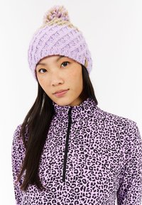 Gorro de punto lila con textura acanalada y pompón beige en la parte superior. Se lleva con un top morado de estampado de leopardo con cuello alto y cremallera.