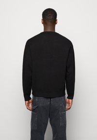 Pull noir à col rond, manches longues et poignets côtelés. Porté avec un pantalon cargo noir avec plusieurs poches.