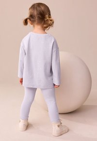 Svetlofialová košeľa s dlhým rukávom s potlačou hviezd, doplnená o zodpovedajúce legíny a biele vysoké tenisky. Jednoduché pozadie s veľkou guľou.