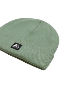 Groene gebreide beanie met een geribbelde textuur en een opgevouwen boord. Heeft een zwart rechthoekig label met het woord "PROTEST."