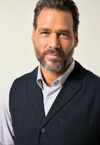 Mörkblå ullväst för män med notch-lapel, enkel knappstängning och bröstficka över en ljusrutig skjorta.