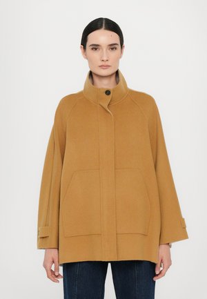 Cappotto in lana color cammello con colletto alto, maniche raglan e due tasche frontali. Presenta una chiusura a bottoni nascosta e una vestibilità ampia.