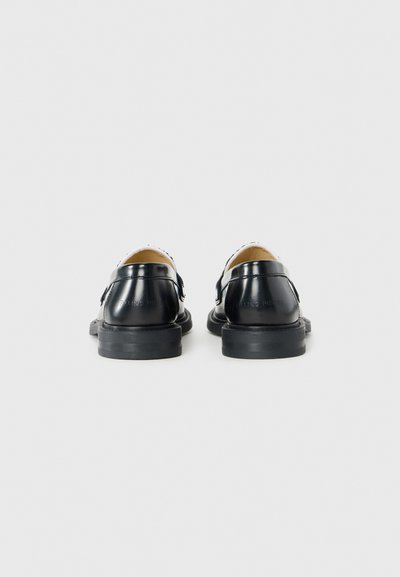 Black leather shoes with a smooth finish, rounded shape, low heel, and decorative stitching along the edges. Minimalist design with no embellishments.