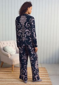 Tamsiai mėlynas pižamos komplektas su šviesiai rožiniu gėlių raštu. Su ilgomis rankovėmis ir laisvais kelniais. Minkšta, lygi medžiaga.