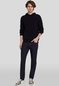 Zwarte hoodie met aantrektouwen, gecombineerd met donkerblauwe jeans en zwart-witte sneakers, gepresenteerd op een neutrale achtergrond.