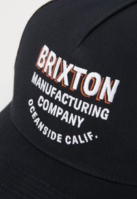 Fekete sapka hímzett szöveggel: "BRIXTON MANUFACTURING COMPANY OCEANSIDE CALIF." fehér és narancssárga színben. Klasszikus baseball stílusú dizájn.