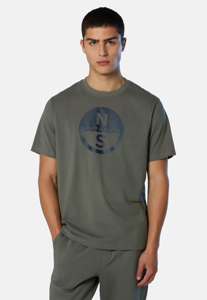 T-shirt à manches courtes vert olive en coton, avec un logo circulaire bleu marine portant les inscriptions "NORTH SAILS" et "N S" sur le devant.
