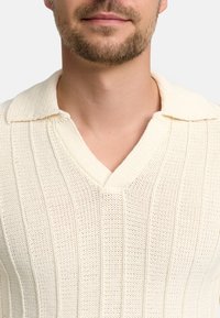 Maglione a maglia in bianco sporco con texture a coste verticali, design a V e colletto piatto. Materiale leggero e traspirante.
