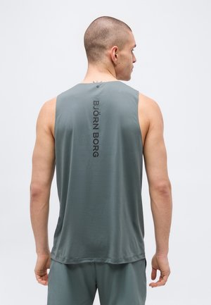 Mees paljaste päid ja halli varrukateta spordisärgis ning lühikestes pükstes, näidates tagasi, millel on vertikaalne "BJÖRN BORG" tekst.