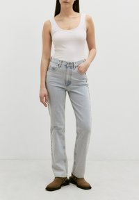 Lichtblauwe hoge spijkerbroeken met een rechte snit, voorzien van voorzakken en een rits. Gecombineerd met een getailleerde witte tanktop en bruine muiltjes.