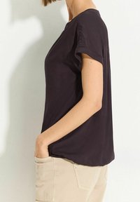 Haut noir à manches courtes avec une coupe décontractée, une texture lisse, un col rond et un pli subtil dans le dos, associé à un pantalon beige clair.