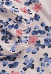 Blommig tyg med ljusrosa botten och blåa och rosa blommönster. Samlad elastisk detalj vid kanten, mjuk textur.