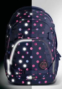 Backpack featuring a navy blue fabric with pink and blue polka dots. Includes reflective accents and straps, with a logo patch on the front.