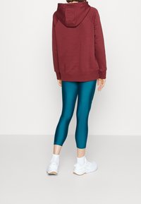 Felpa con cappuccio color bordeaux abbinata a leggings turchesi, caratterizzata da una texture elastica e liscia. Scarpe da ginnastica bianche completano l'outfit.