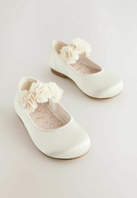 Ballerines en satin blanc avec bout arrondi, petit talon, ornées de fleurs en tissu couleur crème sur la bride. Semelle intérieure texturée.