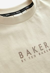 Beżowa bawełniana koszulka z okrągłym dekoltem, z subtelnym wytłoczonym logo "BAKER by TED BAKER" w ciemniejszym odcieniu na środku przodu.