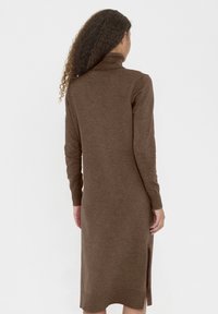 Barna kötött ruha magasított gallérral, hosszú ujjakkal, oldalsó hasítékkal és testhez simuló sziluettel, puha textúrával. Hátsó nézet látható.