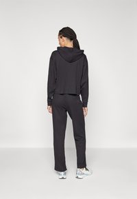 Črn skrajšani hoodie s kapuco, kombiniran s ohlapnimi črnimi hlačami in patterned supergami. Material se zdi mehak in udoben.