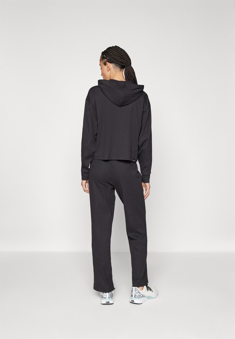 Felpa nera corta con cappuccio, abbinata a pantaloni neri larghi e sneakers con fantasia. Il materiale sembra morbido e confortevole.