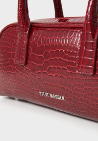 Rød faux læder håndtaske med krokodille tekstur, rund form og dobbelte top håndtag. Har sølvfarvet branding på fronten.