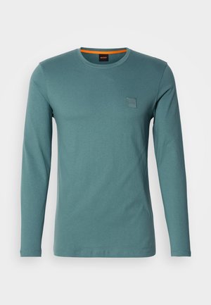 Langärmliges Rundhals-Shirt in Tealfarbe. Hergestellt aus weicher Baumwolle, mit einem kleinen quadratischen Logo-Patch oben links. Glatte Textur, lässiges Design.