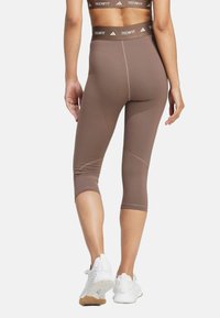Braune, taillierte Leggings mit einem figurbetonten Design und einem kontrastierenden Bund, der "TECHFIT" zeigt. Tragen mit weißen Sportschuhen.