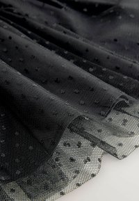 Schwarzer transparenter Stoff mit erhabener Punktstruktur, sanft gefaltet, um das geschichtete Netzmuster und die Halbtransparenz auf einem weißen Hintergrund zu zeigen.
