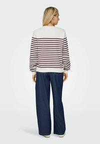 Sweatshirt rayé crème et bordeaux, avec un col rond et des poignets côtelés, associé à un jean en denim foncé à pattes larges.