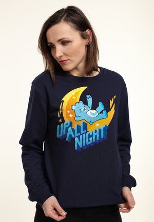 Námořnický svetr s kruhovou grafikou zobrazující modrého medvěda a nápisem "UP ALL NIGHT" tučným, gradientním písmem. Měkký materiál, volný střih.