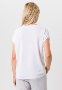 Witte top met korte mouwen en een gestructureerd, geweven patroon. Ronde halslijn en een losse pasvorm, gecombineerd met lichtgrijze broeken.