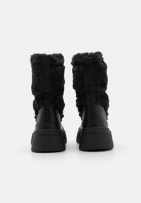 Black ankle boots with faux fur lining, a smooth leather exterior, thick rubber sole, and adjustable straps at the back.