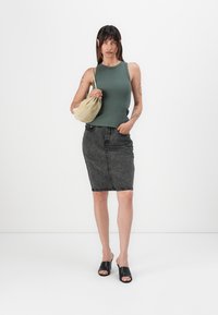 Grønn ermeløs topp kombinert med et svart denim blyantskjørt. Tilbehøret inkluderer en lyse farget veske og svarte slip-on sandaler.