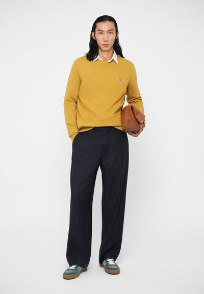 Κίτρινο πουλόβερ, λευκό γιακά, ναυτικές παντελόνες με ρίγες, πράσινα αθλητικά παπούτσια με λευκές κορδόνες, κρατώντας μια καφέ υφασμάτινη τσάντα. Απλός, καθαρός σχεδιασμός.