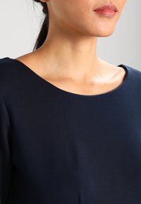 Granatowa bluzka z szerokim, okrągłym dekoltem i gładką fakturą. Materiał wydaje się lekki i dopasowany do górnej części ciała.