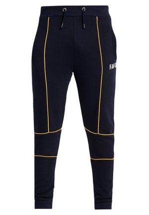 Pantaloni da jogging blu navy con dettaglio piping giallo, vita con coulisse, polsini a coste e testo bianco parziale sulla parte superiore della coscia.