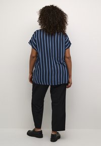 Chemise bleu marine avec des rayures verticales bleu clair, manches courtes et ourlet arrondi. Associée à un pantalon noir et des chaussures noires robustes.