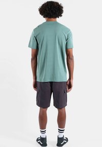 T-shirt vert clair à manches courtes en coton. Associé à un short cargo foncé et des chaussettes rayées. Les chaussures sont noires avec des accents blancs.