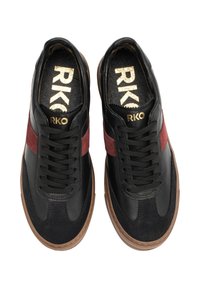 Ein Paar schwarze Turnschuhe mit roten Wildleder-Seitenstreifen, braunen Sohlen, schwarzen Schnürsenkeln und goldener "RKO"-Markierung auf den Einlegesohlen und Zungen.