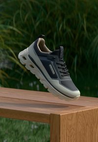 Svarte og grå sneakers med en teksturert mesh-overdel og gummisåle, med en fremtredende polstret mellomsåle og snøresystem.