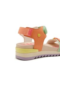 Sanda de múltiples colores con una parte superior sintética naranja, correa ajustable y una suela texturizada de múltiples capas en púrpura, amarillo y rosa.