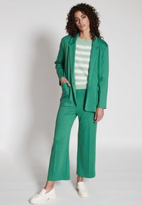 Grön blazer, matchande gröna vida byxor och en ljusgrön randig tröja. Vita slip-on skor fulländar outfiten. Slät textur.