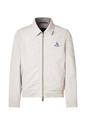 Chaqueta beige con cremallera y cuello, dos bolsillos laterales y un pequeño logotipo bordado en azul en el lado izquierdo del pecho.