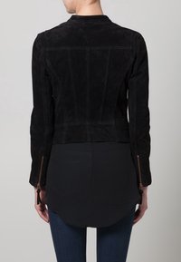 Zwarte suède jas met een nauwsluitend ontwerp, naden aan de achterkant en ritssluitingen aan de manchetten. Bleke stiksels accentueren de strakke lijnen en gevormde silhouet.