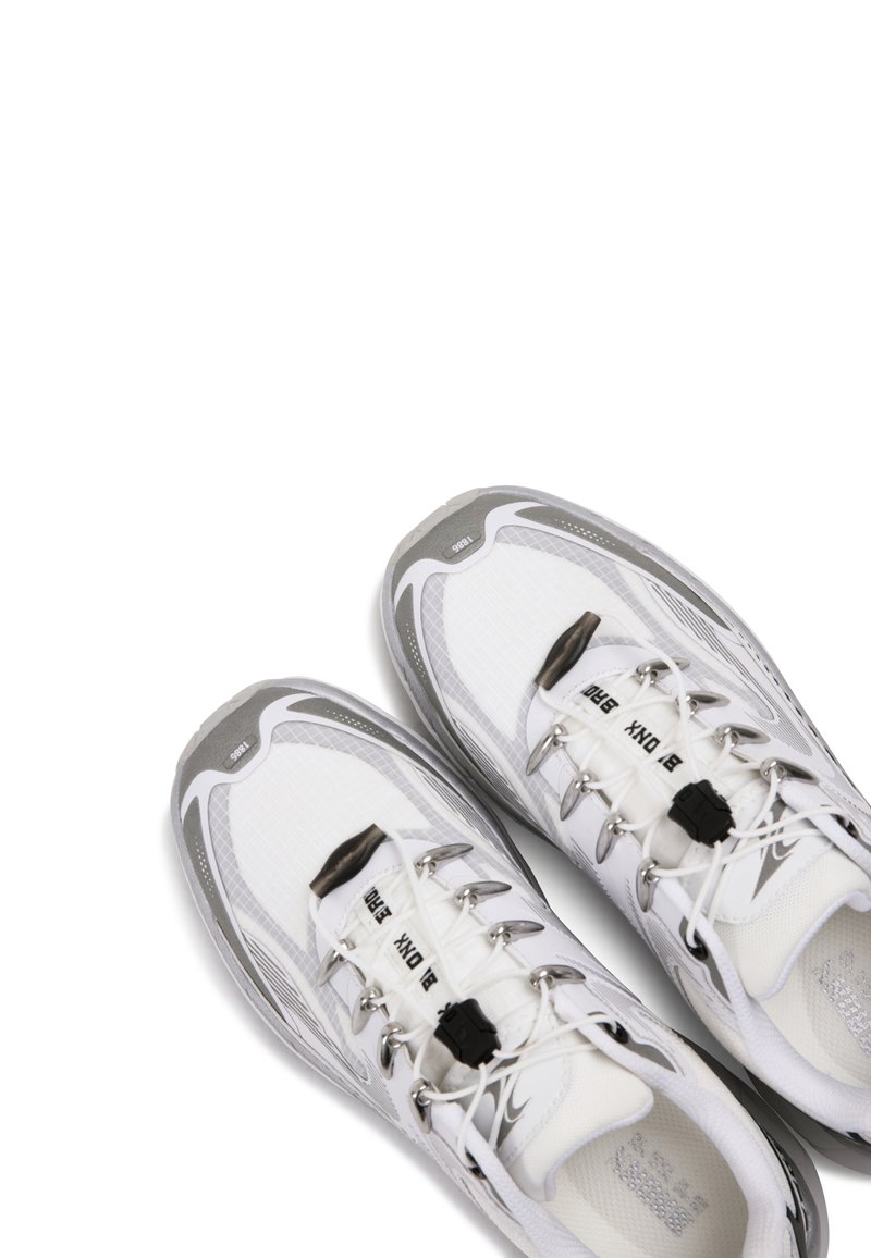 Un par de zapatillas deportivas blancas y grises con sistema de cordones rápidos y cierres de cordones negros sobre un fondo blanco.