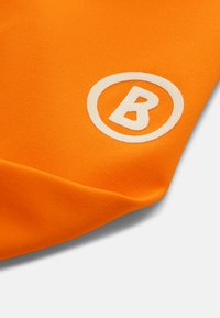 Orange stof med en glat tekstur, der har et hvidt cirkulært logo med et "B" i midten. Synlig syning langs kanten.
