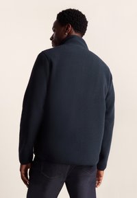 Dark navy fleece jacket with a high collar, textured surface, long sleeves, and a relaxed fit. No visible hardware or accents.