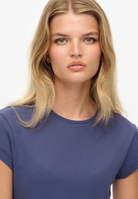 Camiseta de color azul marino con mangas cortas, cuello redondo y tela de algodón suave. El modelo tiene el cabello largo y rubio y un maquillaje natural.