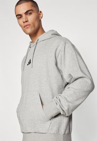 Sweatshirt cinza feito de tecido macio, com um bolso canguru, punhos canelados e um logótipo preto bordado no peito.